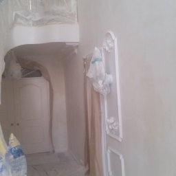 Tyzon Victor Tyszlewicz - Wnętrze po malowaniu na biało, z dekoracyjnymi sztukateriami na ścianie i zabezpieczoną folią podłogą. Widoczny fragment balkonu i drzwi.