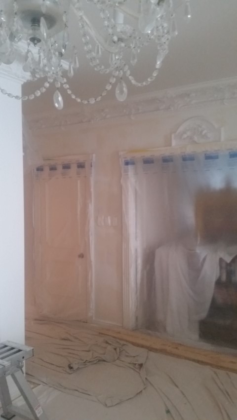 Pokój zabezpieczony folią malarską przed malowaniem, widoczny żyrandol kryształowy i sztukateria. Przygotowania do odświeżenia wnętrza.