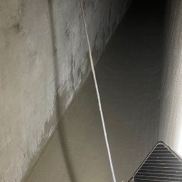 BGCOMPANY - Wnętrze betonowego tunelu po nałożeniu gładzi, widoczne ślady wilgoci i drabina w prawym dolnym rogu. Ujęcie z dołu, podkreślające perspektywę.