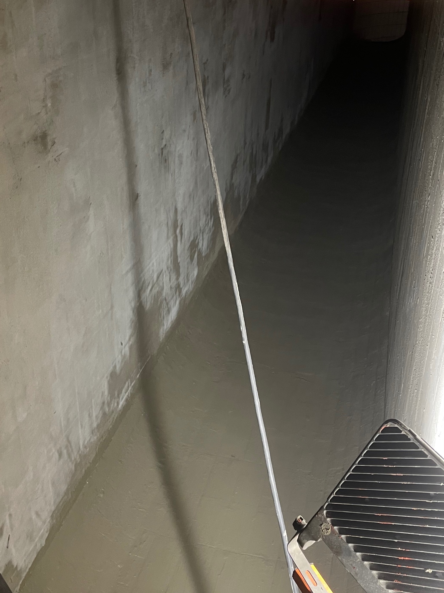 Wnętrze betonowego tunelu po nałożeniu gładzi, widoczne ślady wilgoci i drabina w prawym dolnym rogu. Ujęcie z dołu, podkreślające perspektywę.