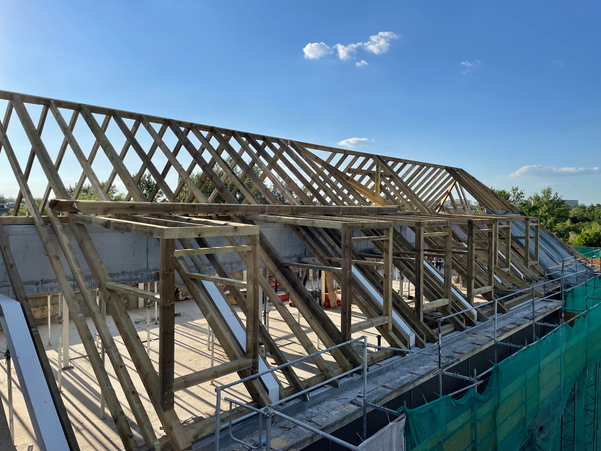 Konstrukcja drewniana dachu w trakcie budowy, widok z góry na rusztowanie, błękitne niebo w tle. Elementy zaimpregnowane, widoczne detale łączeń.