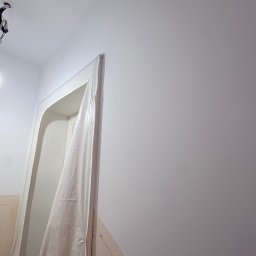 Kacper Starobrzyński - Przygotowanie do malowania: zabezpieczone folią drzwi w jasnym wnętrzu. Widoczne ślady ołówka na ścianie, sufit z instalacją elektryczną. Ujęcie z dołu.