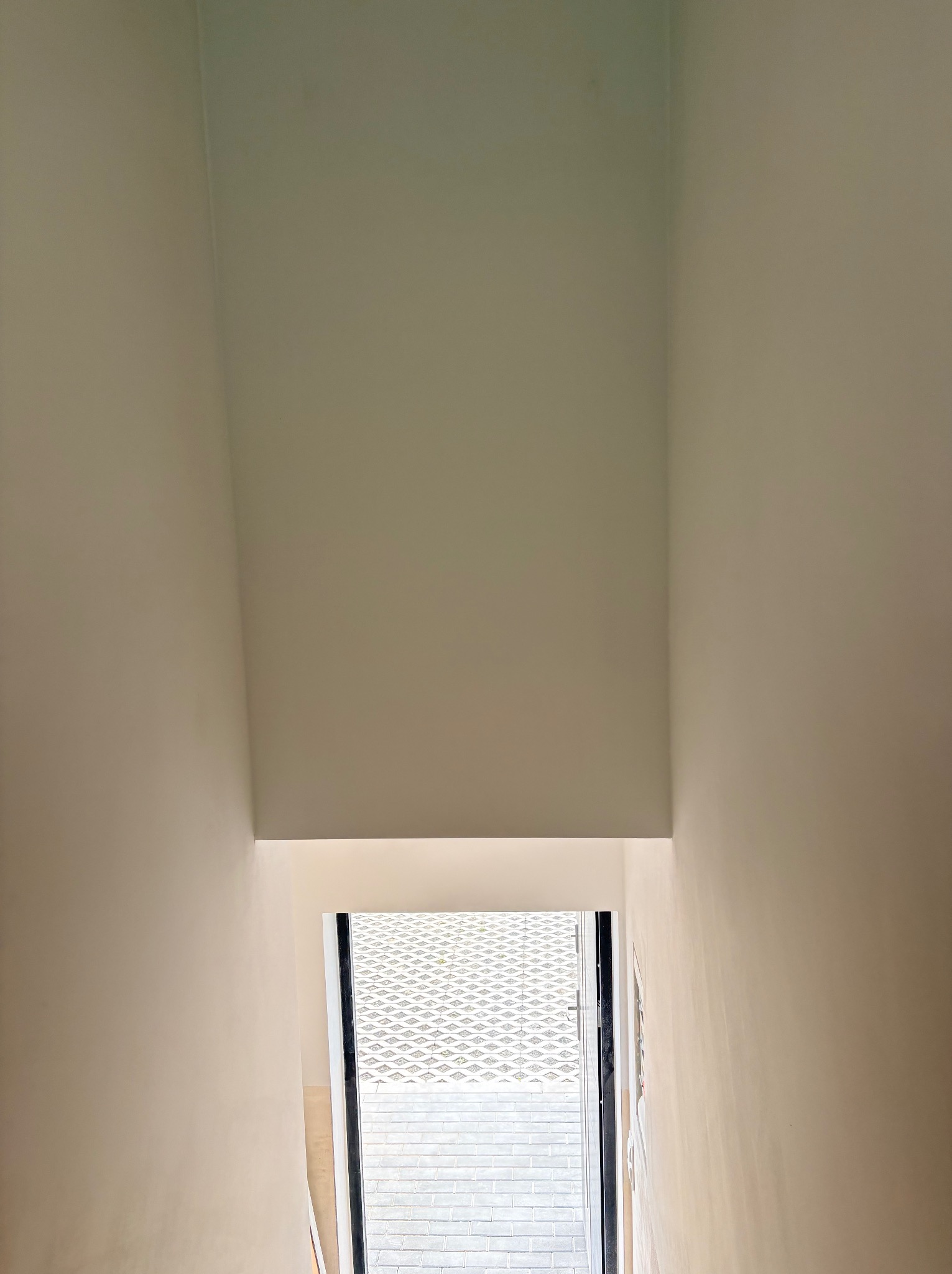 Wnętrze po malowaniu: gładkie, jasne ściany w odcieniach bieli, widok na zewnątrz przez otwarte drzwi. Minimalistyczny design, świeżo odnowione pomieszczenie.