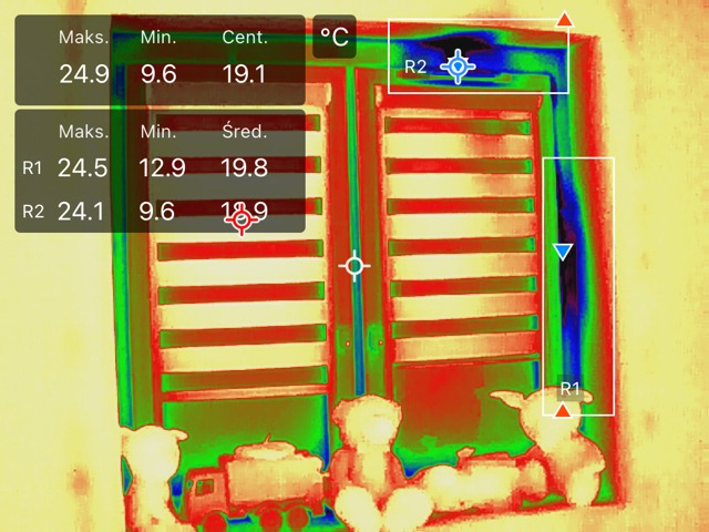 Termowizja okna z żaluzjami i zabawkami na parapecie, z zaznaczonymi obszarami pomiaru temperatury (R1, R2) i wyświetlonymi wartościami minimalnymi, maksymalnymi i średnimi.