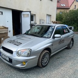 ELBI plus Arkadiusz Pacan - Srebrny samochód Subaru Impreza z naklejonym logo 'elbipius' na masce i boku, zaparkowany na żwirowym podjeździe przed budynkiem z otwartymi drzwiami garażowymi.