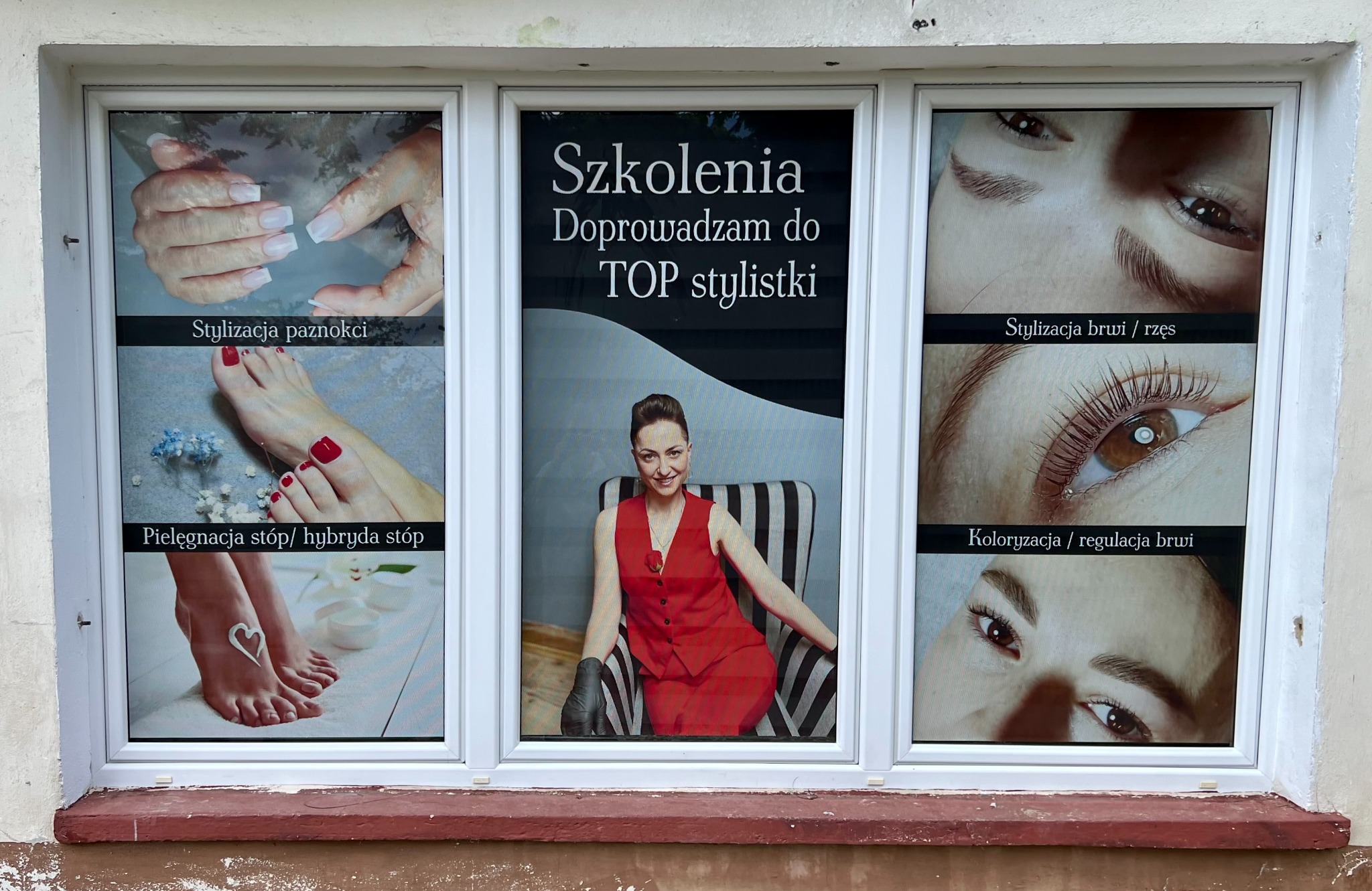 Okna salonu z reklamami: stylizacja paznokci, pielęgnacja stóp, szkolenia dla stylistek, stylizacja brwi i rzęs, koloryzacja brwi. Widok z zewnątrz.