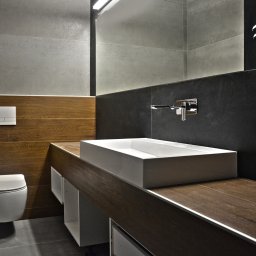 Kristobal Design - Nowoczesna łazienka z drewnianymi akcentami: prostokątna umywalka nablatowa, szare płytki i podwieszana toaleta. Minimalistyczny design z oświetleniem LED.