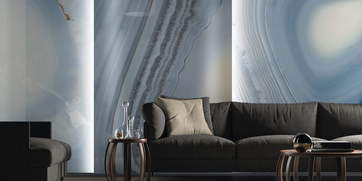 Stylowy salon z szarą sofą i stolikami na tle ściany z efektem agatu w odcieniach błękitu i szarości. Nowoczesne lampy po bokach ściany.