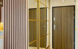 Nowoczesna szafa wnękowa z lustrzanymi drzwiami i złotymi ramami, dopasowana do przedpokoju z drewnianymi lamelami i brązowymi drzwiami wejściowymi.