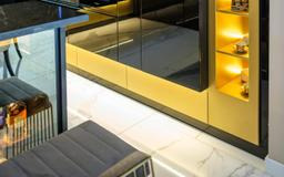 Nowoczesna zabudowa kuchenna z czarnymi, błyszczącymi frontami i złotymi akcentami, oświetlona od dołu, z widocznym fragmentem wyspy i krzesła barowego.