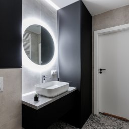 ARVION GROUP SP. Z O.O. - Nowoczesna łazienka z podświetlanym lustrem, białą umywalką na czarnym blacie i wzorzystą podłogą. Minimalistyczny design z szarymi płytkami i białymi akcentami.