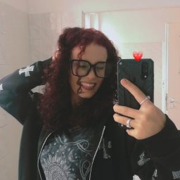 Wiktoria Karczewska - Uśmiechnięta kobieta z kręconymi włosami w okularach robi selfie w łazience, ubrana w bluzę z krzyżami i koszulkę z motywem słońca i księżyca.