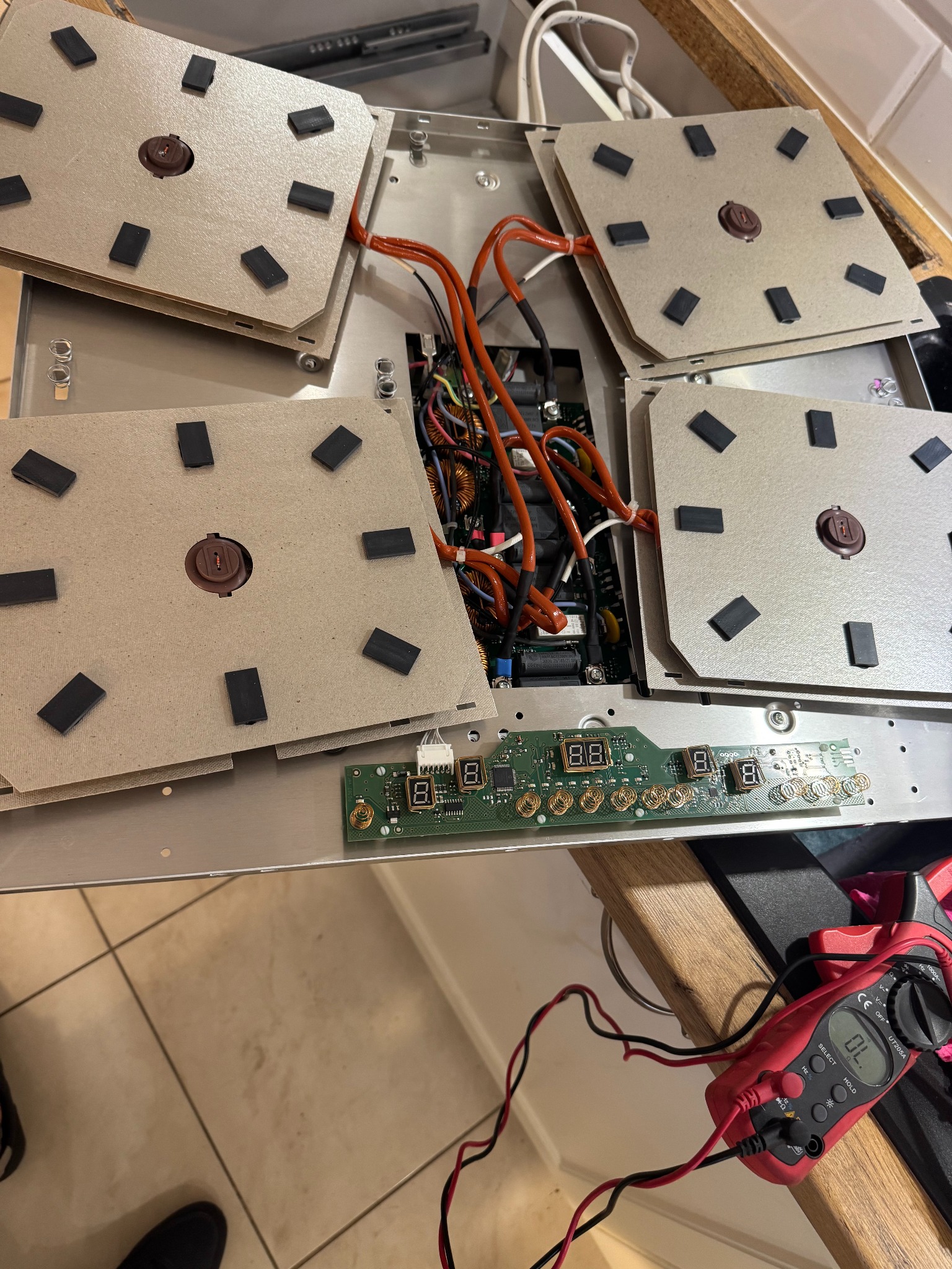 Rozłożona płyta indukcyjna z widocznymi elementami grzejnymi, elektroniką i miernikiem. Widoczne kable i podzespoły. Sprzęt AGD w trakcie naprawy.