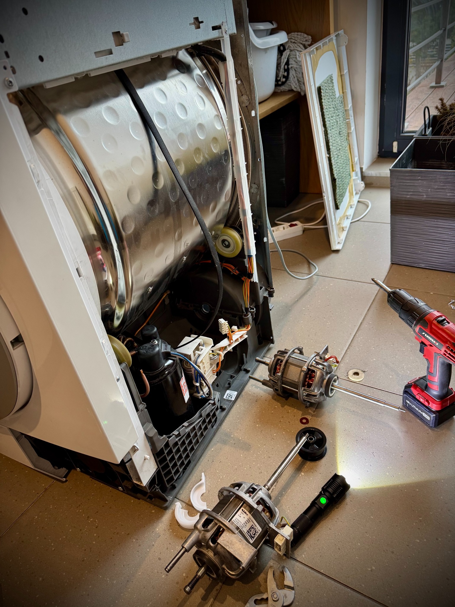 Rozłożona pralka z widocznymi elementami silnika i narzędziami w Chrzanowie. Widoczne wnętrze bębna i elementy obudowy. Praca w toku, oświetlenie punktowe.