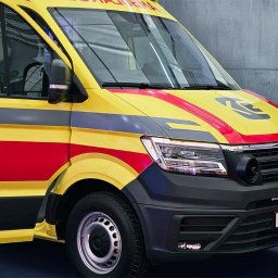 KG Special Performance - Żółto-czerwony ambulans Volkswagen Crafter z widocznym logo Special Performance na tle betonowej ściany. Ujęcie z przodu, skupione na detalu.