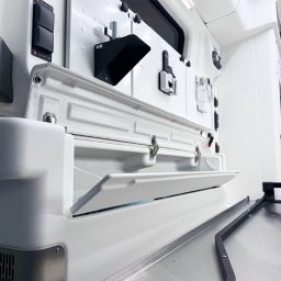 KG Special Performance - Wnętrze specjalistycznego pojazdu z otwartą, białą szafką i elementami wyposażenia, w tym czarne przełączniki i uchwyty, sugerujące zaawansowaną instalację elektryczną.