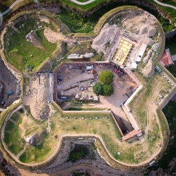 DRONAM dron*foto*film - Fort w trakcie renowacji, widok z drona. Zewnętrzne wały ziemne porośnięte trawą, wewnątrz plac budowy z maszynami i materiałami. Unikalny kształt gwiazdy.