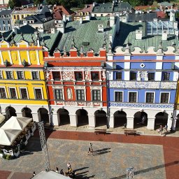 DRONAM dron*foto*film - Kolorowe kamienice z podcieniami na Rynku Wielkim w Zamościu, widok z góry. Czerwona cegła placu, białe parasole restauracji. Ujęcie z drona.