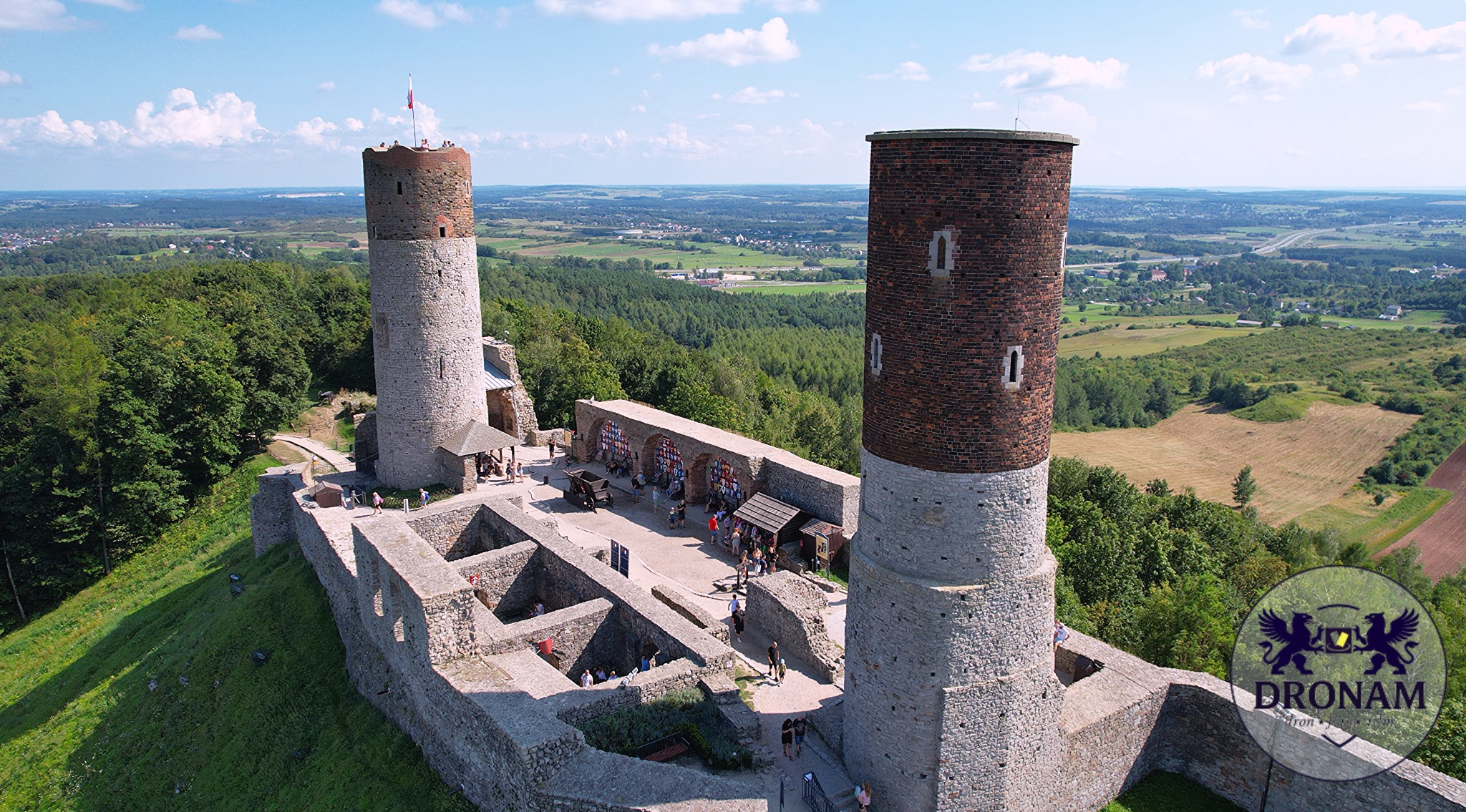 Panorama zamku w Chęcinach z lotu ptaka, dwie wieże, dziedziniec z turystami, otoczenie zieleni i krajobrazu. Ujęcie z drona w słoneczny dzień.