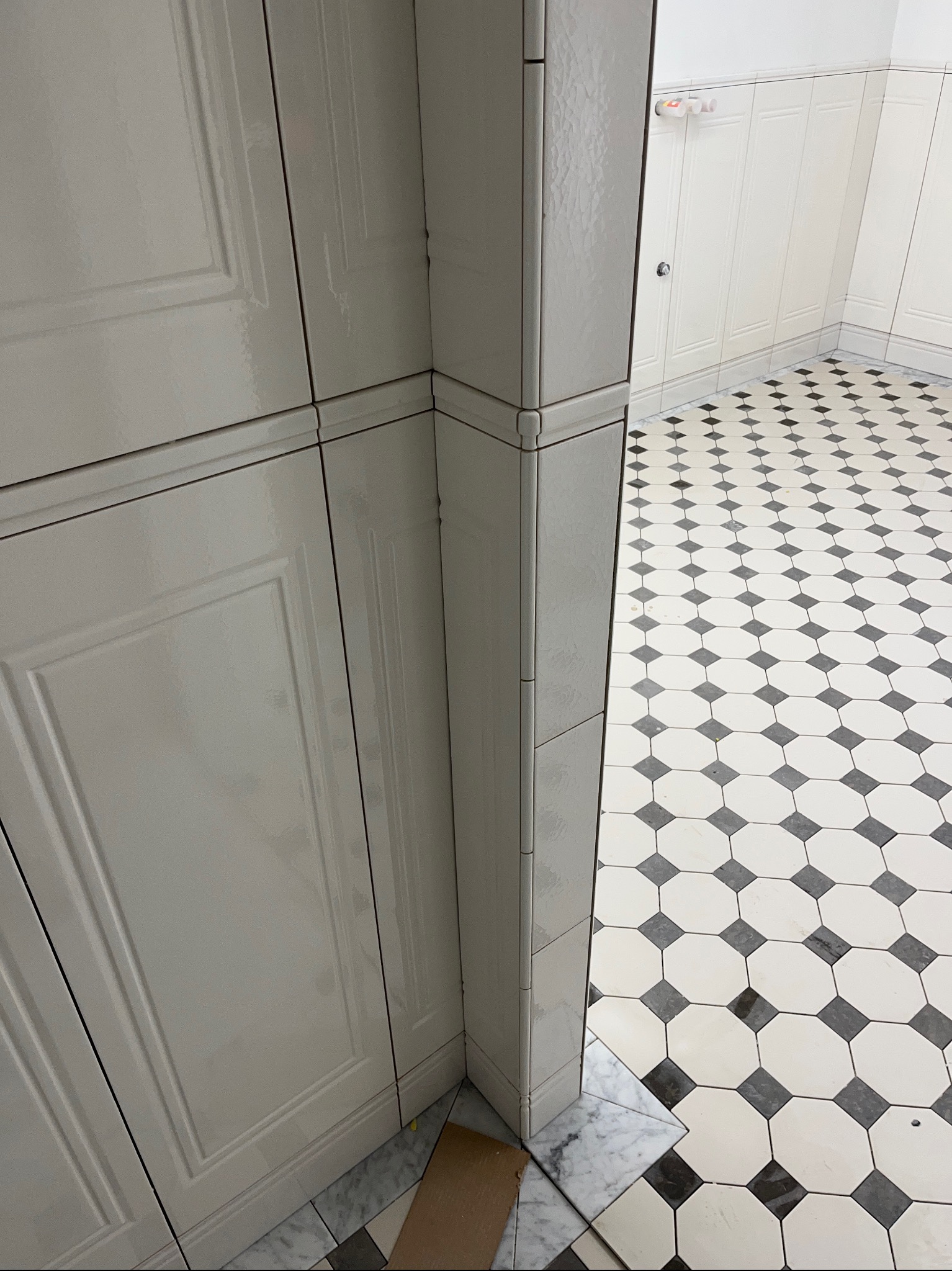 Biała zabudowa meblowa w łazience z dekoracyjnymi płytkami podłogowymi w czarno-białą szachownicę. Klasyczny styl wykończenia wnętrza.