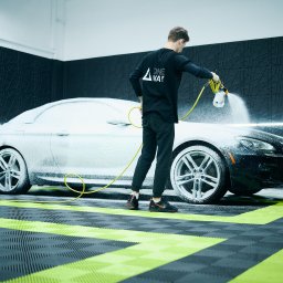 One Way Detailing - Czyszczenie pianą aktywnej na czarnym BMW serii 6 w nowoczesnej myjni z wzorzystą ścianą i podłogą. Pracownik w czarnym uniformie spryskuje auto.