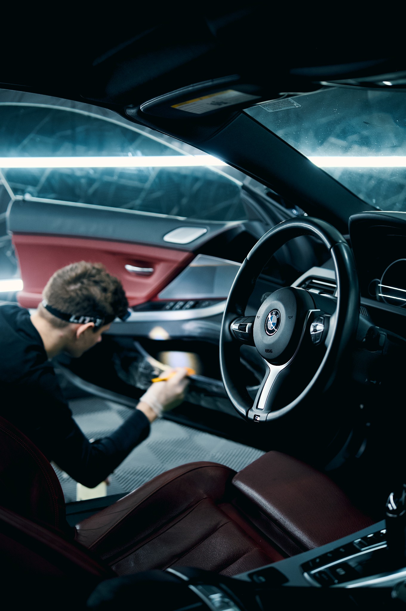 Wnętrze BMW: detailer w rękawicach czyści szczotką boczek drzwi. Widoczna kierownica, skórzane fotele i oświetlenie LED. Auto detailing w profesjonalnym studiu.
