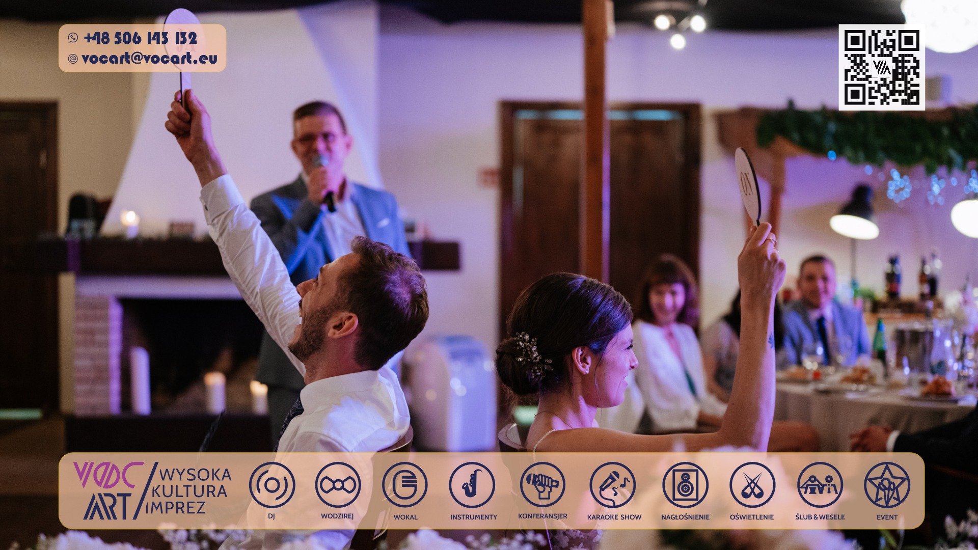 Para młoda wznosi tabliczki z napisem 'ON' podczas wesela, wodzirej z mikrofonem w tle. Dekoracje i oświetlenie tworzą radosną atmosferę.