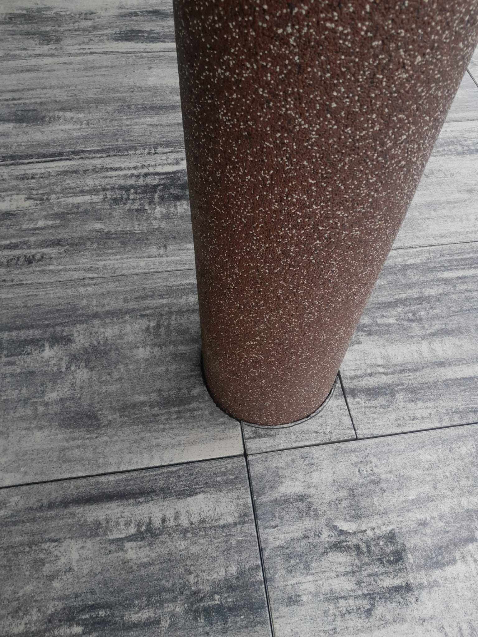 Szara kostka brukowa z efektem drewna, obok brązowa donica. Widok z góry, ukazujący detale faktury i ułożenie kostki. Realizacja z dbałością o estetykę.