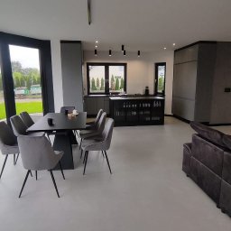 GW Projekt Grzegorz Worobiej - Nowoczesne wnętrze z szarą posadzką, prawdopodobnie mikrocement, stół z krzesłami i częściowo widoczna sofa. Minimalistyczne oświetlenie sufitowe.