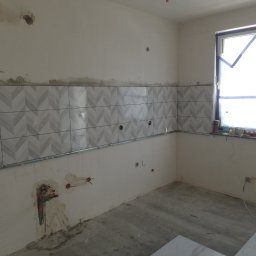 Jacek Szczepański - Montaż płytek w kuchni: wzór w jodełkę na ścianie, widoczne niedokończone prace, surowy stan podłogi, okno zabezpieczone folią malarską.