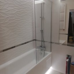 Jacek Szczepański - Nowoczesna łazienka po remoncie: biała wanna z parawanem, dekoracyjne płytki 3D na ścianie, oświetlenie LED pod wanną, grzejnik drabinkowy w lustrze.