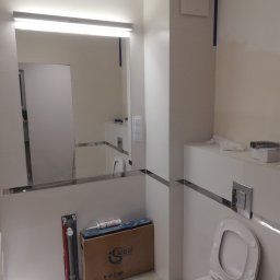 Jacek Szczepański - Nowoczesna łazienka w bieli z toaletą, lustrem z podświetleniem i elementami wykończenia w chromie. Widoczne narzędzia i materiały instalacyjne.