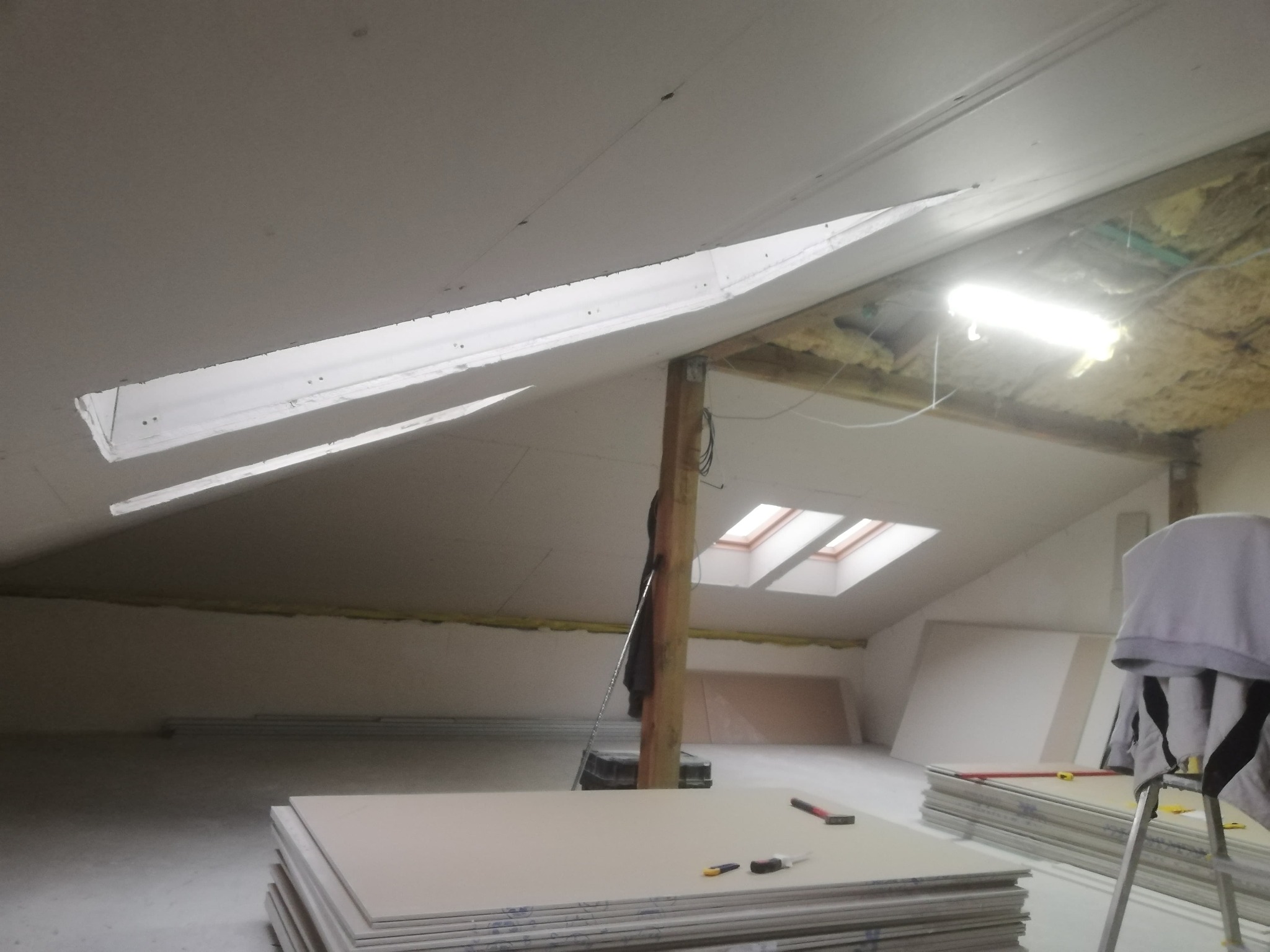 Montaż płyt gipsowo-kartonowych na poddaszu w Markach. Widoczne płyty, narzędzia i oświetlenie. Prace wykończeniowe w trakcie realizacji.