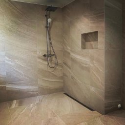 Gerard Wojewoda - Beżowa kabina prysznicowa z deszczownicą i odpływem liniowym. Płytki imitujące marmur, wnęka w ścianie. Minimalistyczny design, nowoczesne wykończenie.