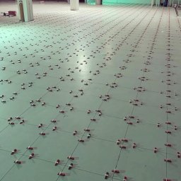 Gerard Wojewoda - Układanie płytek podłogowych z użyciem klipsów poziomujących w dużej przestrzeni. Prace wykończeniowe w Poznaniu, widok z góry, równomierne rozmieszczenie elementów.