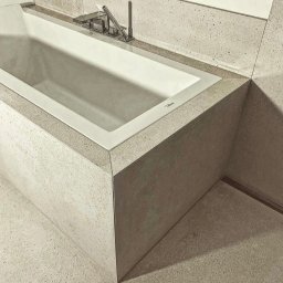 Gerard Wojewoda - Minimalistyczna, biała wanna w obudowie z beżowego kamienia z delikatnym wzorem, nowoczesna armatura, widok z góry, łazienka w neutralnej kolorystyce.