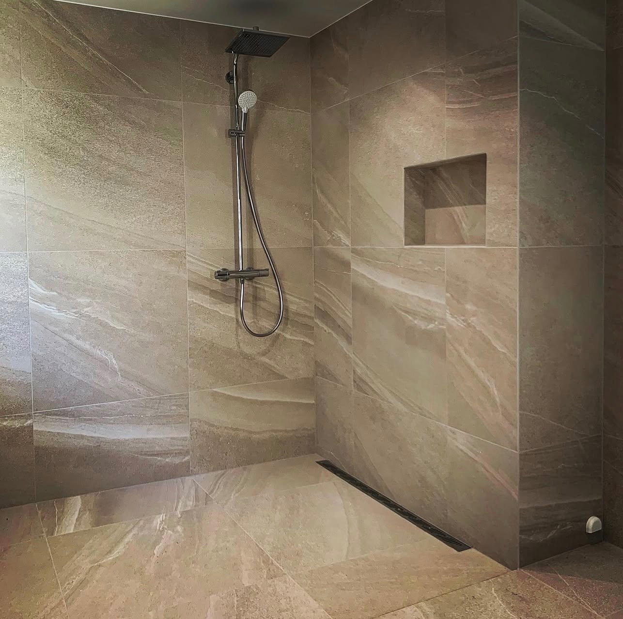 Beżowa kabina prysznicowa z deszczownicą i odpływem liniowym. Płytki imitujące marmur, wnęka w ścianie. Minimalistyczny design, nowoczesne wykończenie.