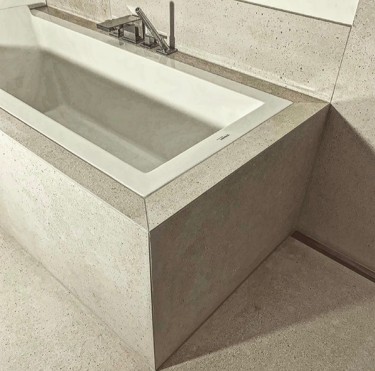 Minimalistyczna, biała wanna w obudowie z beżowego kamienia z delikatnym wzorem, nowoczesna armatura, widok z góry, łazienka w neutralnej kolorystyce.