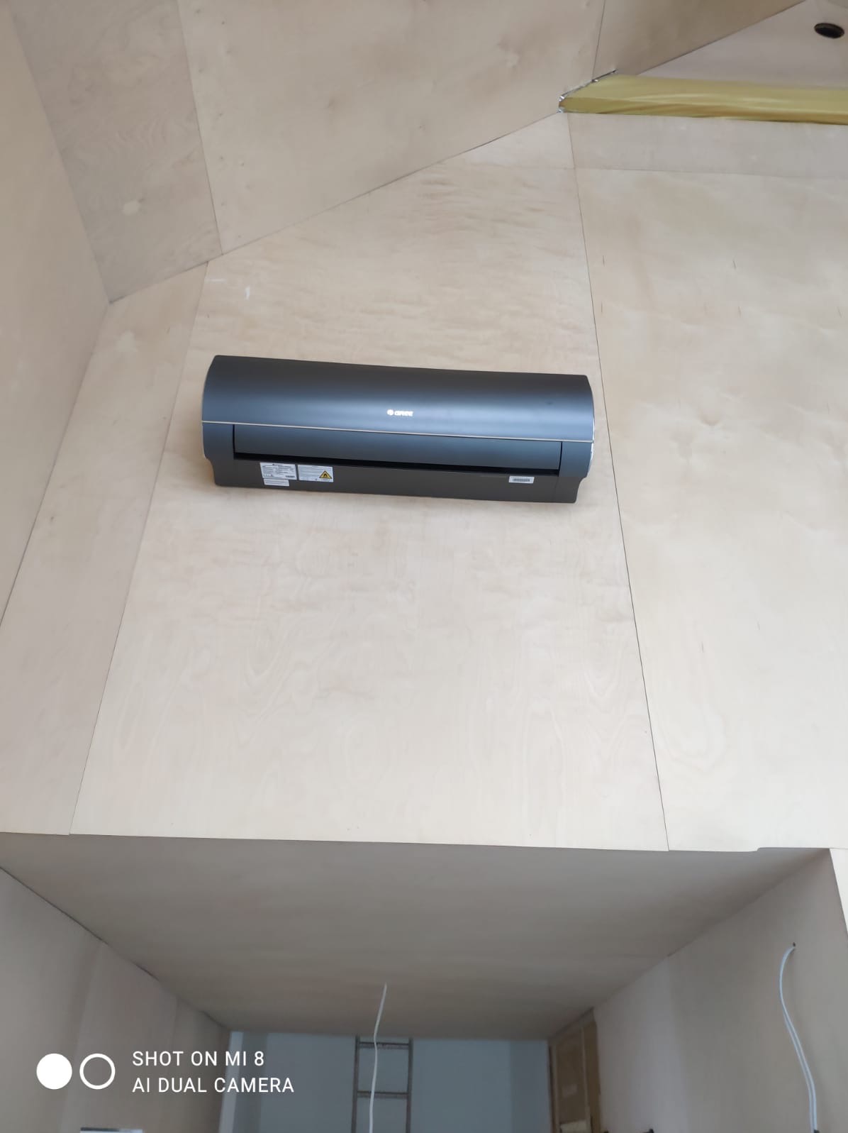 Czarny klimatyzator Gree zamontowany na ścianie w Chorzowie. Widoczne drewniane wykończenie wnętrza i fragment sufitu. Ujęcie z dołu.