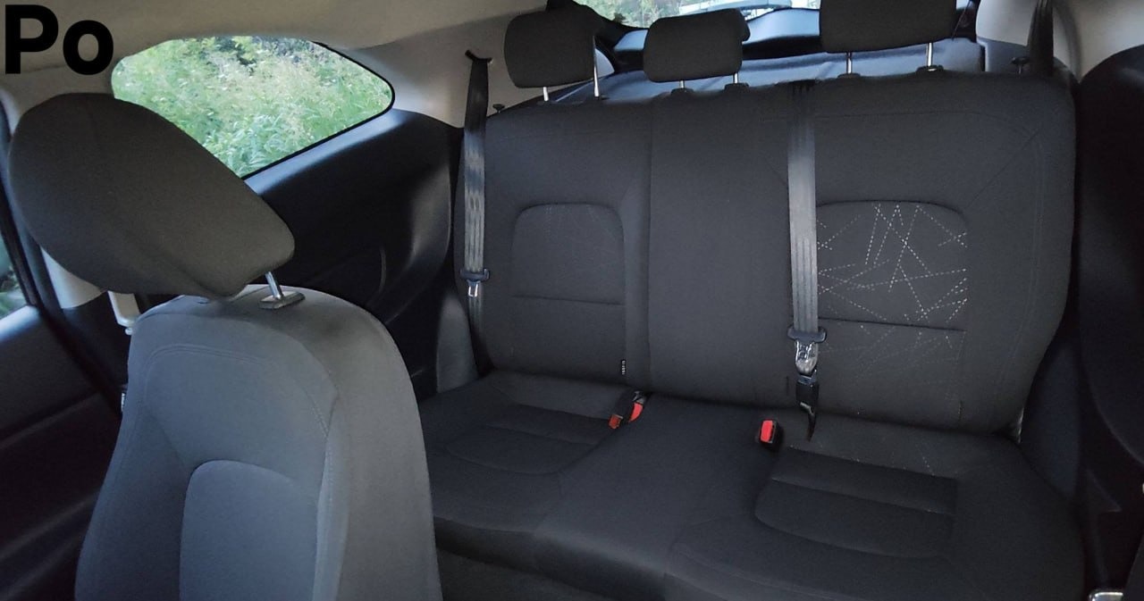 Wnętrze samochodu po czyszczeniu tapicerki. Widoczne tylne siedzenia z wyczyszczoną tapicerką w odcieniach szarości. Na oknie widoczny napis 'Po'.