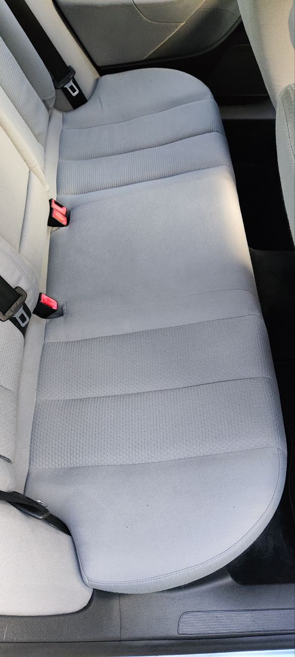 Jasnoszara, tekstylna tapicerka tylnej kanapy samochodowej z widocznymi pasami bezpieczeństwa i zagłówkami, po czyszczeniu.
