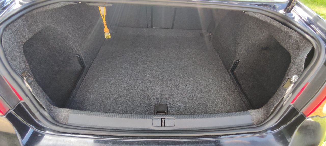 Wnętrze bagażnika samochodu wyłożone szarą wykładziną, widok z góry. W tle widoczny element mocujący w kolorze żółtym. Czysta i zadbana przestrzeń bagażowa.