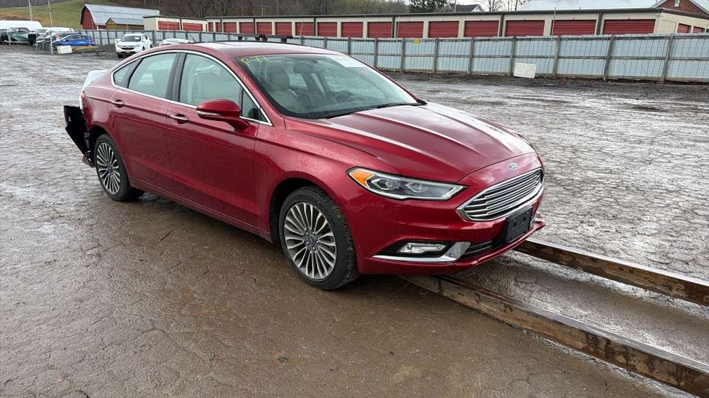 Czerwony Ford Fusion z uszkodzonym tyłem, stojący na zewnątrz w Piaskach Brzóstowskich. Widoczne zarysowania i brakujące elementy karoserii.