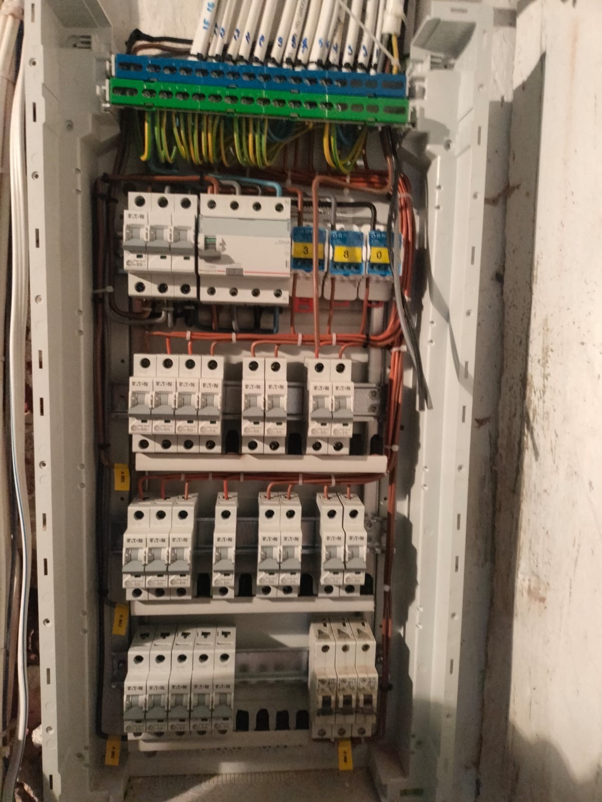 Rozdzielnica elektryczna z bezpiecznikami EATON, okablowaniem i listwami zaciskowymi wewnątrz białej obudowy, zamontowana na ścianie. Widoczne oznaczenia i numery przewodów.