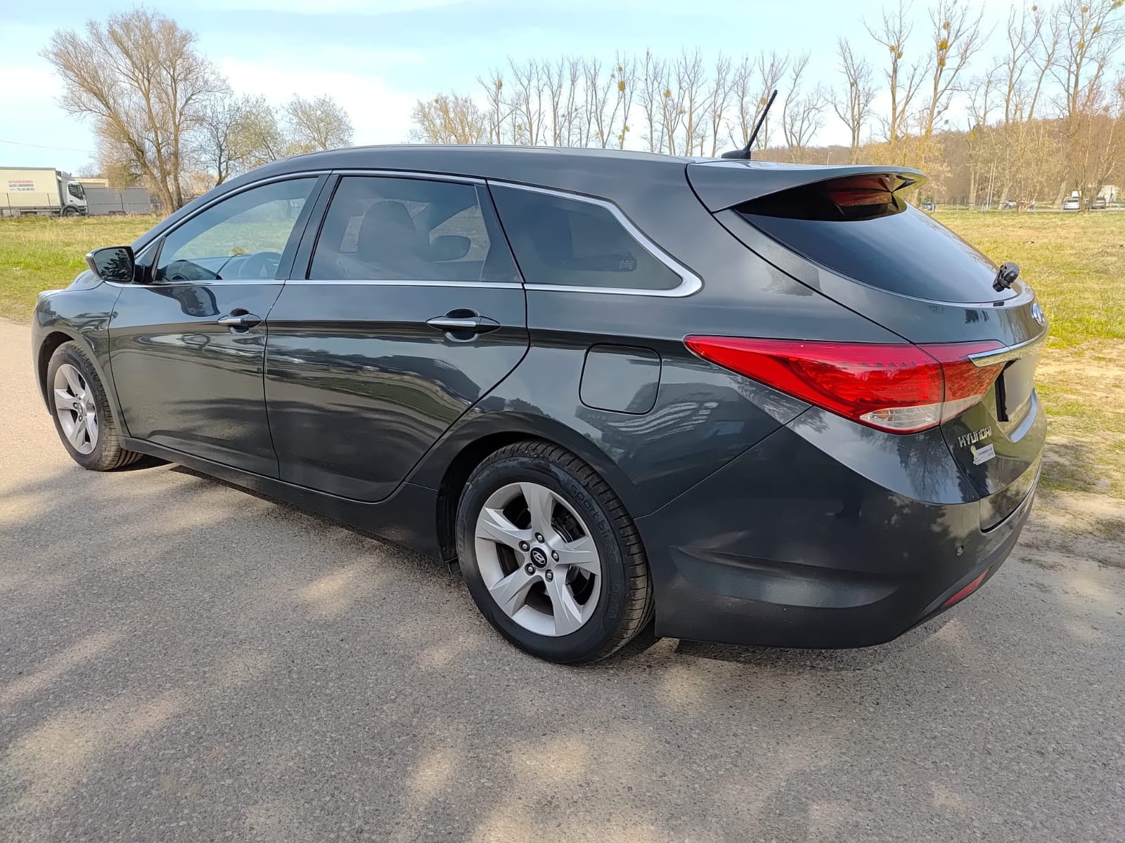 Szary Hyundai i40 kombi po przyciemnianiu szyb, widok z tyłu, lekko z boku. Widoczne ciemne szyby boczne i tylna. Auto stoi na asfalcie, w tle drzewa i trawa.