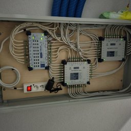 S-Tech Paweł Steć - Rozdzielnica antenowa z multiswitchami i okablowaniem wewnątrz szafki. Widoczne złącza, kable koncentryczne i gniazdko elektryczne z włącznikiem.