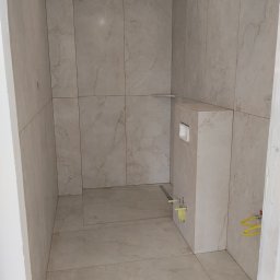 VIKI BUD - Wykończona łazienka z beżowymi płytkami imitującymi marmur, widoczny stelaż podtynkowy WC i odpływ liniowy. Minimalistyczny design, jasne oświetlenie.