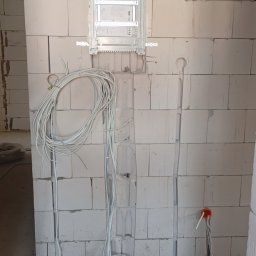Nikodem Nowakowski - Rozdzielnica elektryczna zamontowana na ścianie z betonu komórkowego. Widoczne kable w bruzdach i na podłodze. Etap prac instalacyjnych w surowym stanie.
