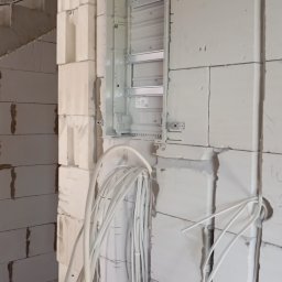 Nikodem Nowakowski - Rozdzielnia elektryczna w surowym stanie, widoczne kable i ściany z betonu komórkowego. Etap prac przed tynkowaniem, z bliska.