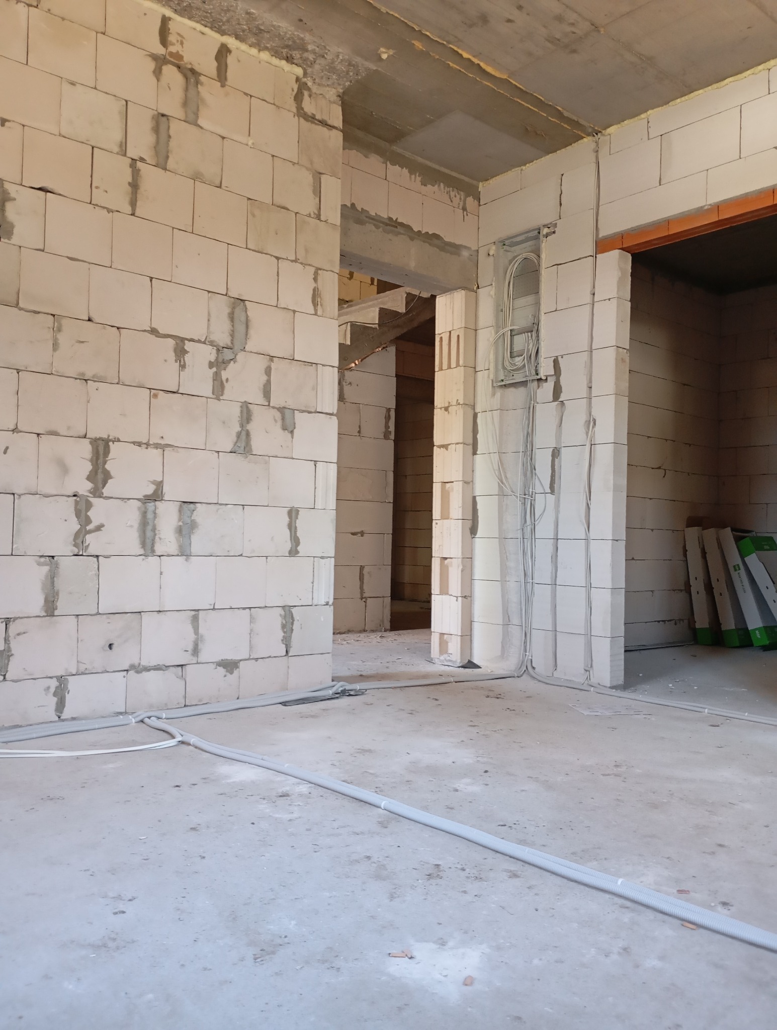 Surowy stan: instalacja elektryczna w peszlach na podłodze, kable w ścianie, ściany z betonu komórkowego, widok na wnętrze w trakcie budowy.
